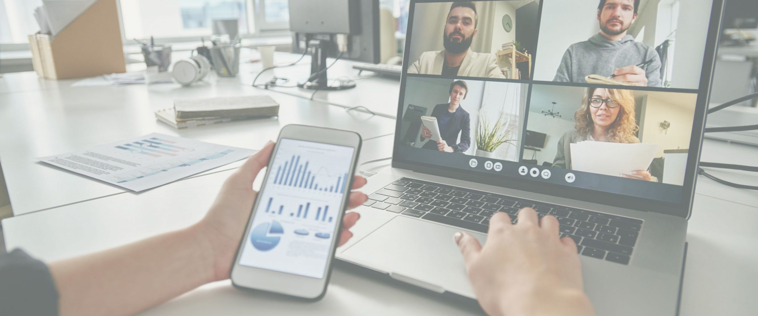 A video meeting on a laptop beside charts on a phone.